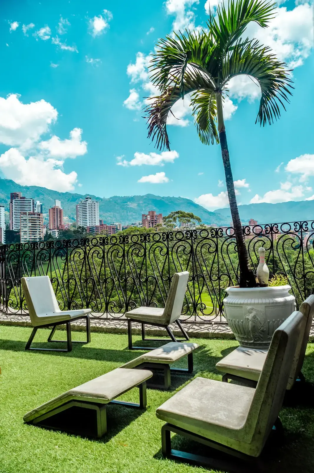 Terraza del Hotel Mantyx en Medellín con sillas, palmera y vista a la ciudad, proyecto de hospedaje de ALUZINA