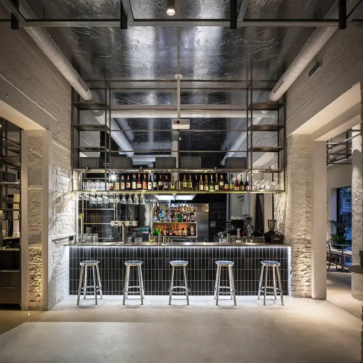 Barra de un espacio diseñado por ALUZINA en Medellín, con taburetes de cromo, muro de ladrillo blanco y ceiling metálico reflectante
