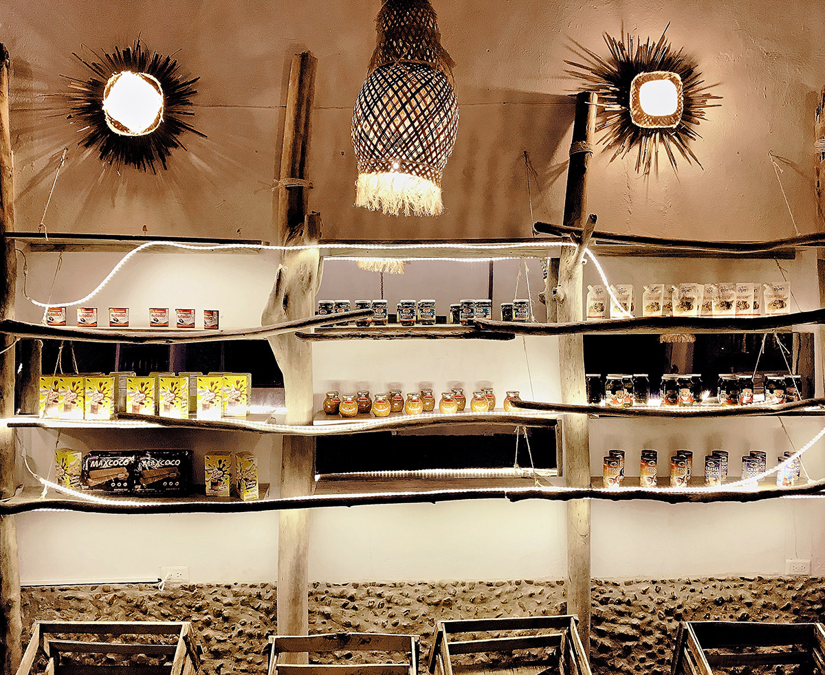 El Bodegón Tropical — espacio comercial y gastronómico en Necoclí con materiales locales, faroles tejidos y estantes rústicos iluminados por Aluzina